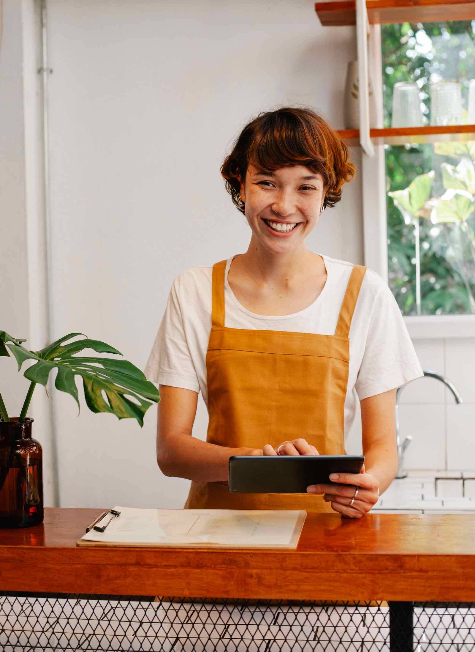 Dueña de un pequeño negocio sonriendo detrás del mostrador de su local mientras usa una tablet
